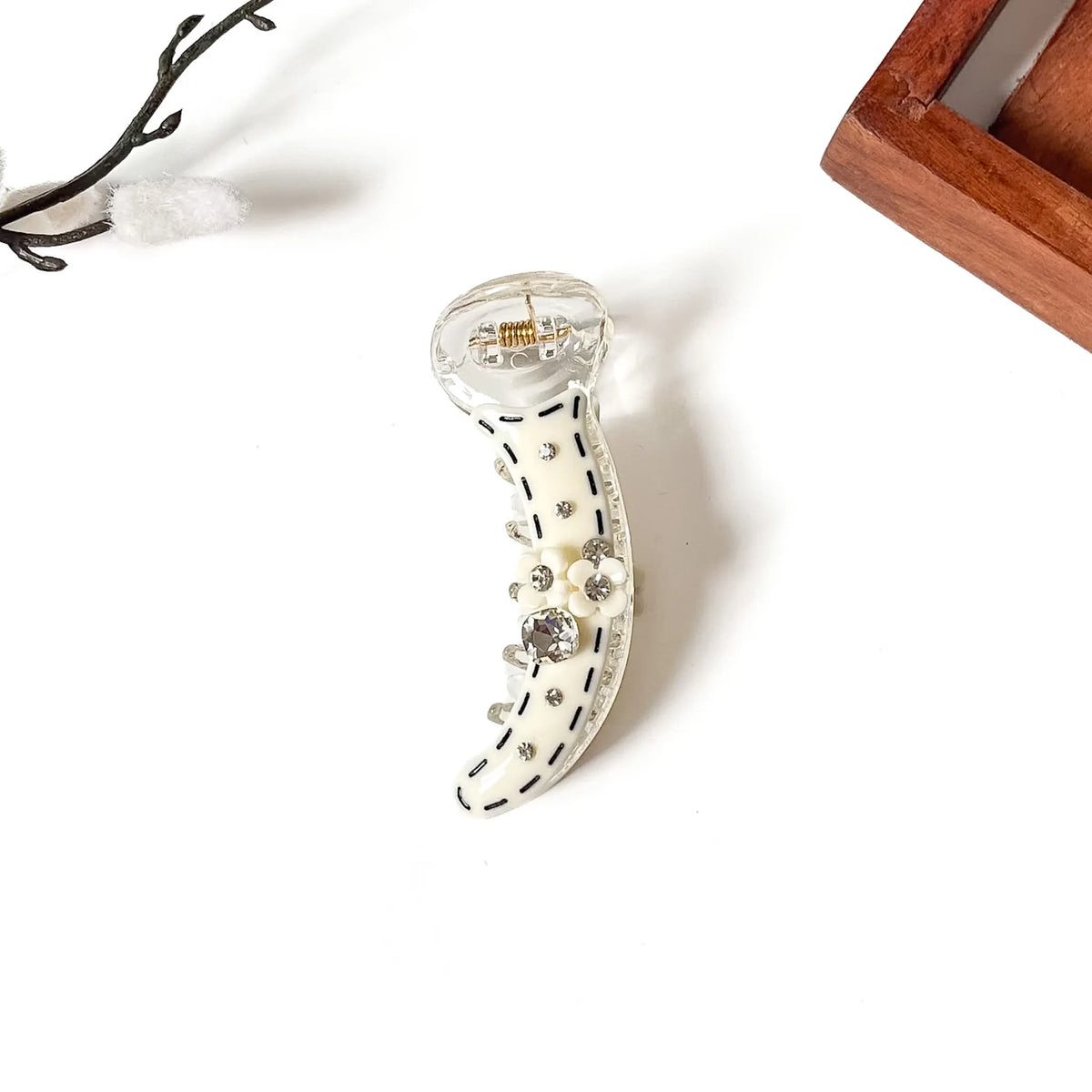 A clear acrylic claw banana clip decorated with an off-white curved body, black dashed line details, and small rhinestones, shown on a white background with decorative props.
