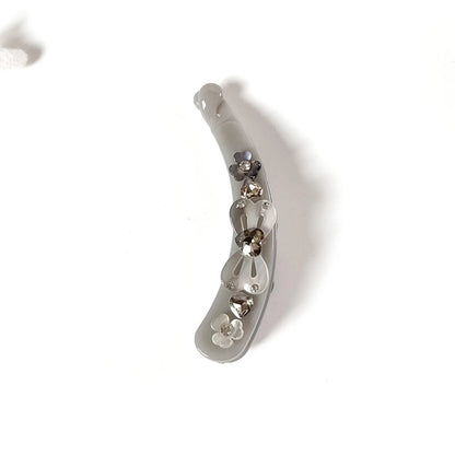 A curved, translucent light gray hair lock banana clip decorated with small metallic silver and gold rhinestones, shown on a plain white background.