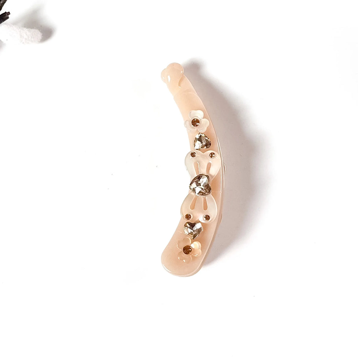 A curved, nude-beige plastic lock banana clip embellished with small metallic gold studs and three clear rhinestones, shown on a plain white background.