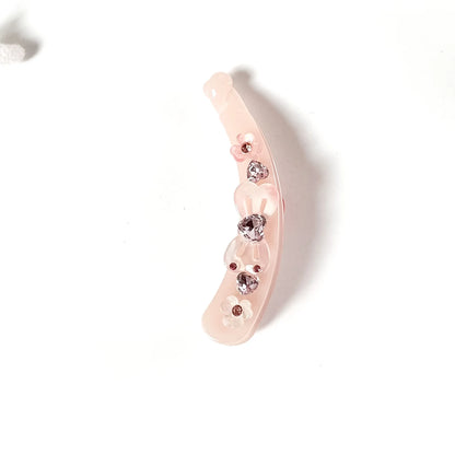 A pale pink curved lock banana clip decorated with small rhinestone flower embellishments, shown on a plain white background.