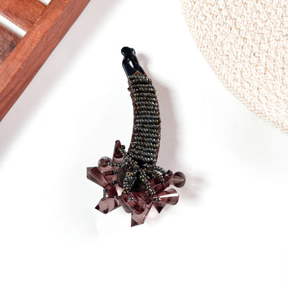 Brown crystalline banana clip with metallic beaded body and oversized rose-gold-toned gemstone embellishment.
