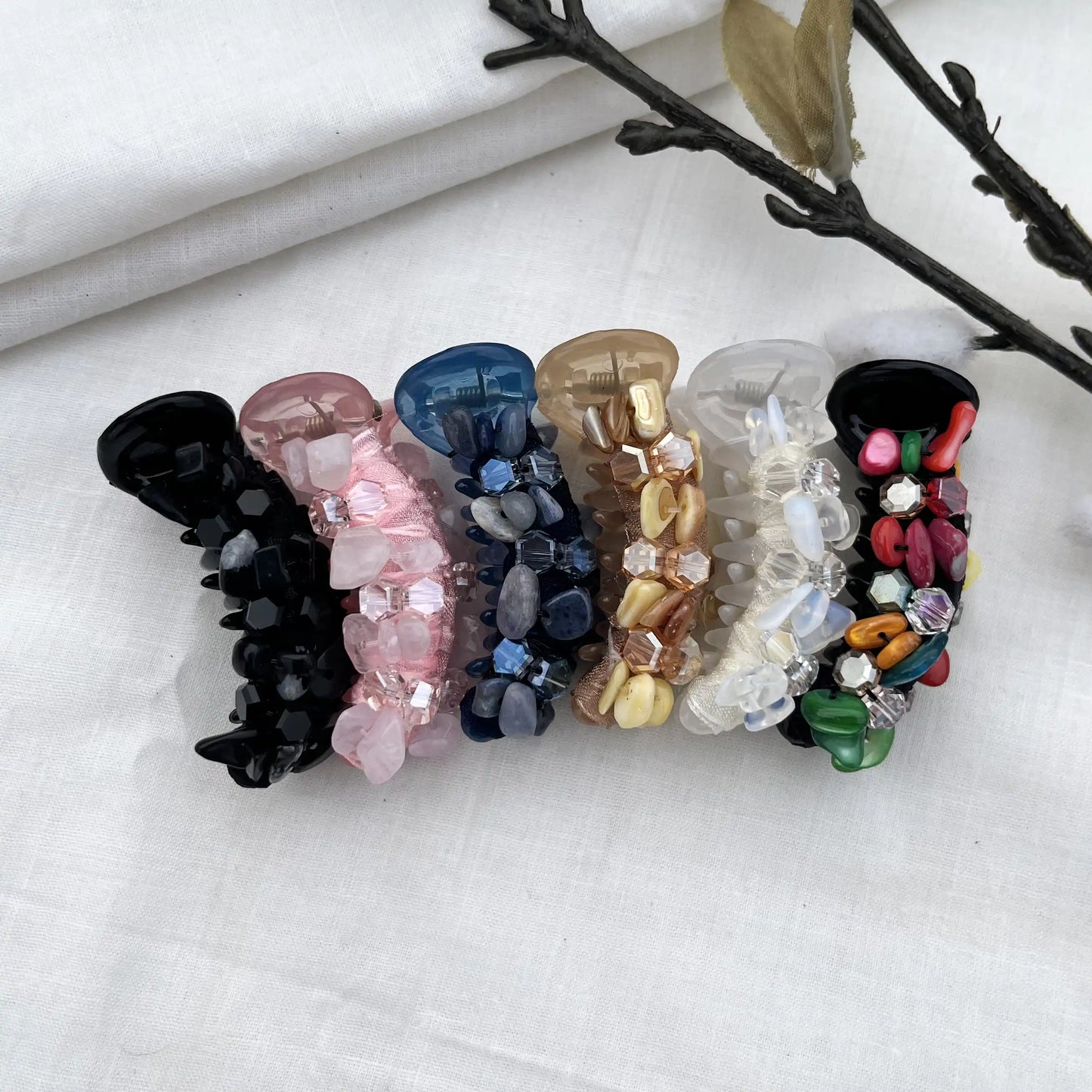 Six dainty mini banana clips in clear crystal, black, blush pink, navy blue, caramel, and multicolor with coordinating faceted beads, arranged flat.
