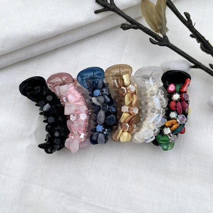 Six dainty mini banana clips in clear crystal, black, blush pink, navy blue, caramel, and multicolor with coordinating faceted beads, arranged flat.