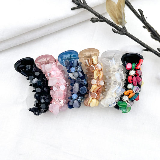 Six dainty mini banana clips in clear crystal, black, blush pink, navy blue, caramel, and multicolor with coordinating faceted beads, arranged flat.