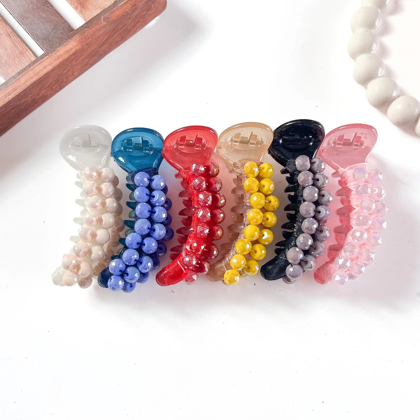 Six dome bead banana clips in cream, cobalt blue, red, caramel, black, and hot pink with faceted dome bead embellishments, arranged flat on cream background.