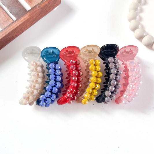Six dome bead banana clips in cream, cobalt blue, red, caramel, black, and hot pink with faceted dome bead embellishments, arranged flat on cream background.
