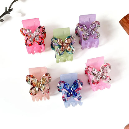 Six butterfly-shaped claw catch clips in assorted pastel and multicolor shades, decorated with rhinestone-embellished wings, arranged on a white background.
