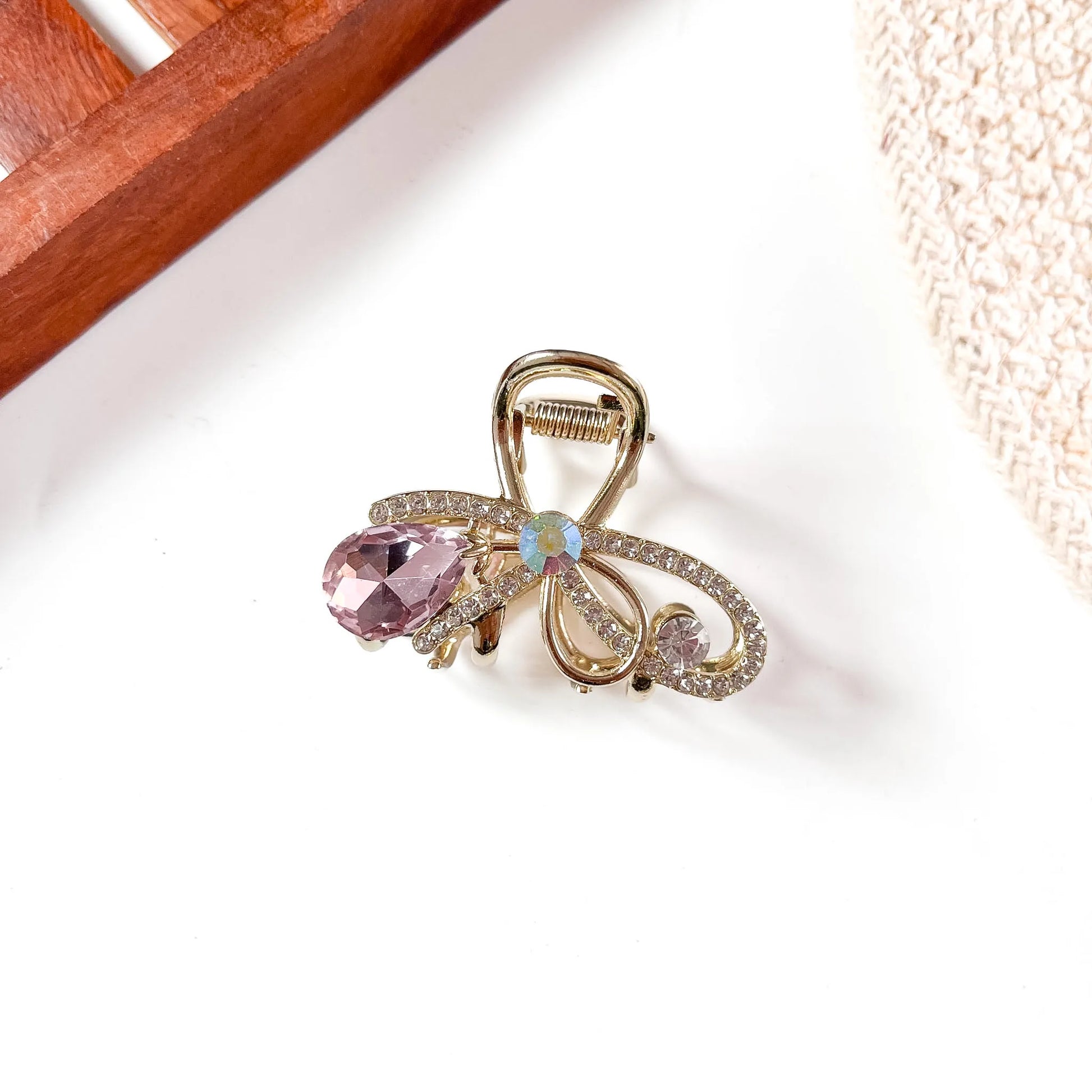 Medium rose pink gemstone metal claw clip featuring ornate gold-tone filigree bow and hanging pink faceted teardrop with opalescent accent stone.