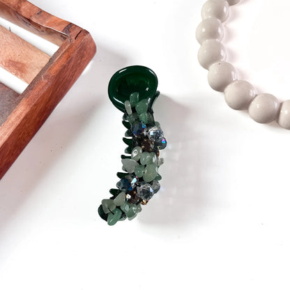 Deep forest green banana clip with large faceted green and mixed-tone gemstone chunks across polished barrel.