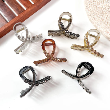 Six large stone claw clips in clear, black, smoky black, caramel, rose gold, and golden amber with rhinestone accents, arranged flat.