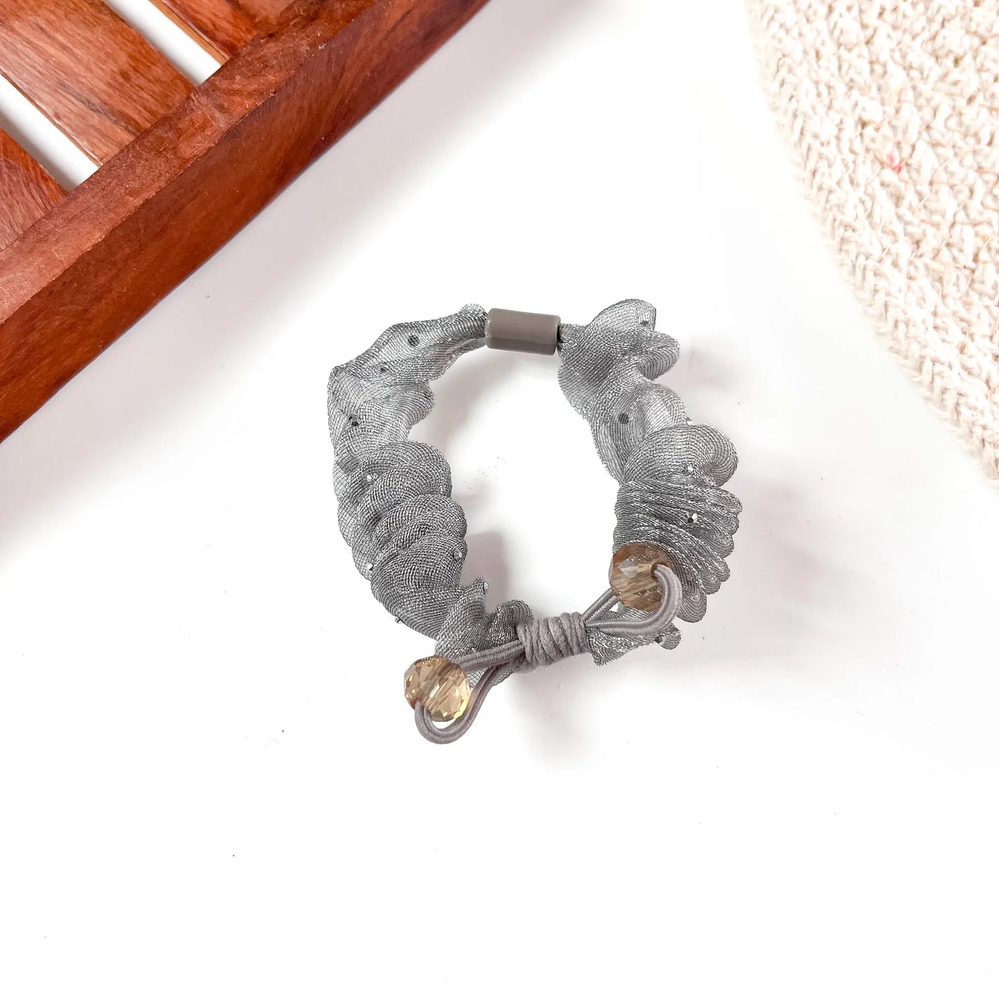 Close-up of a silver metallic organza scrunchie with chunky gathered mesh and gold-tone crystal bead closures.