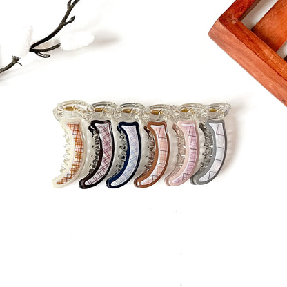 Six clear acrylic claw mini banana clips with different colored grid patterns, arranged in a row on a white background with decorative props.