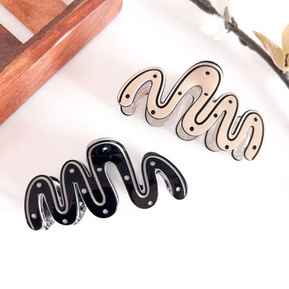 Both sculptural wave clips: ivory and black minimalist wave design with ribbed detailing