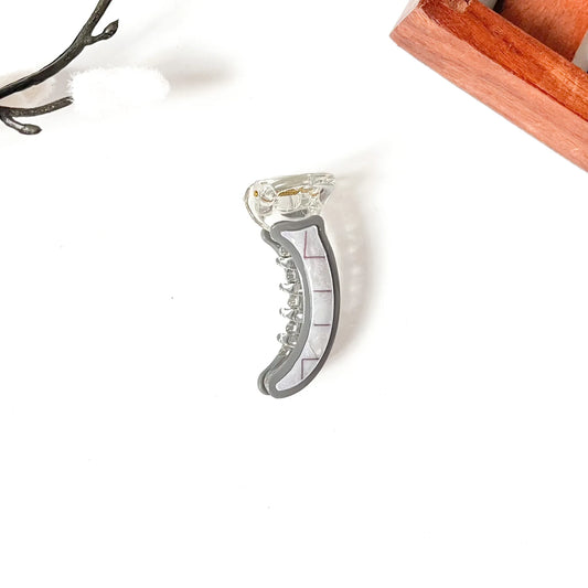 A clear acrylic mini banana clip with a gray inner lining and a white printed measurement scale, shown on a white background with styled props.